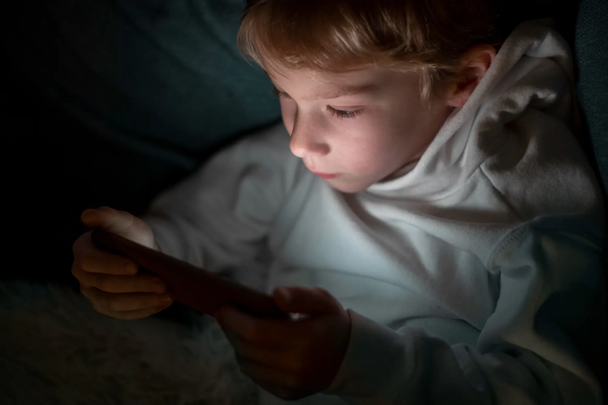Dziecko uzależnione od telefonu – chłopiec wieczorem w ciemności wpatruje się w ekran smartfona